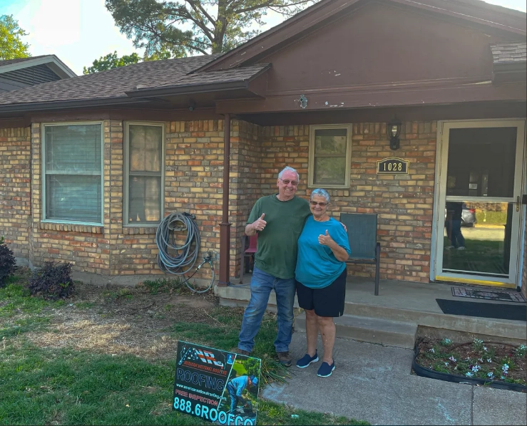 A man and woman with their thumbs up posing in front of their house