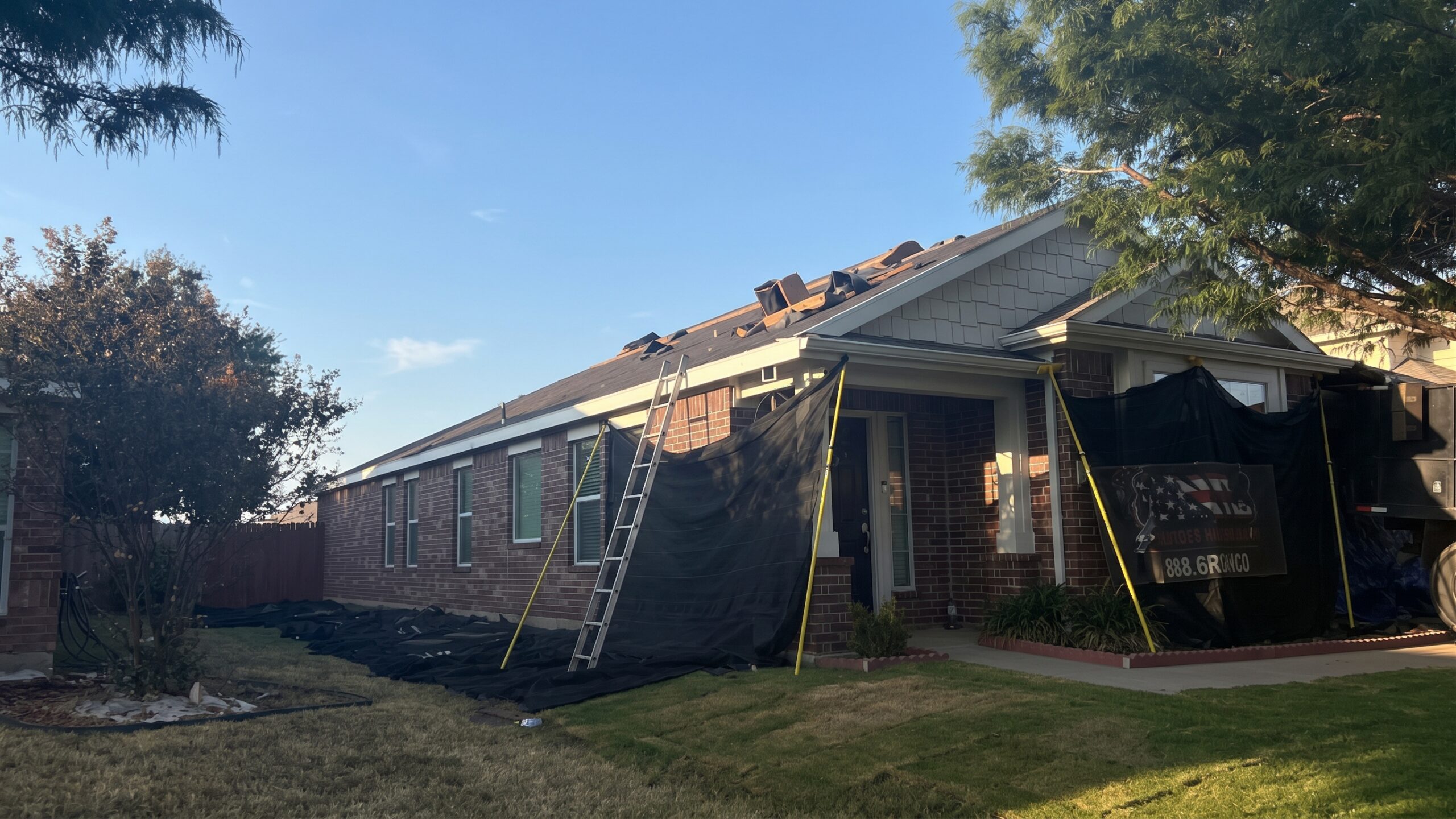 Roofers doing a tear-off with the home's windows and flowers protected by tarps.