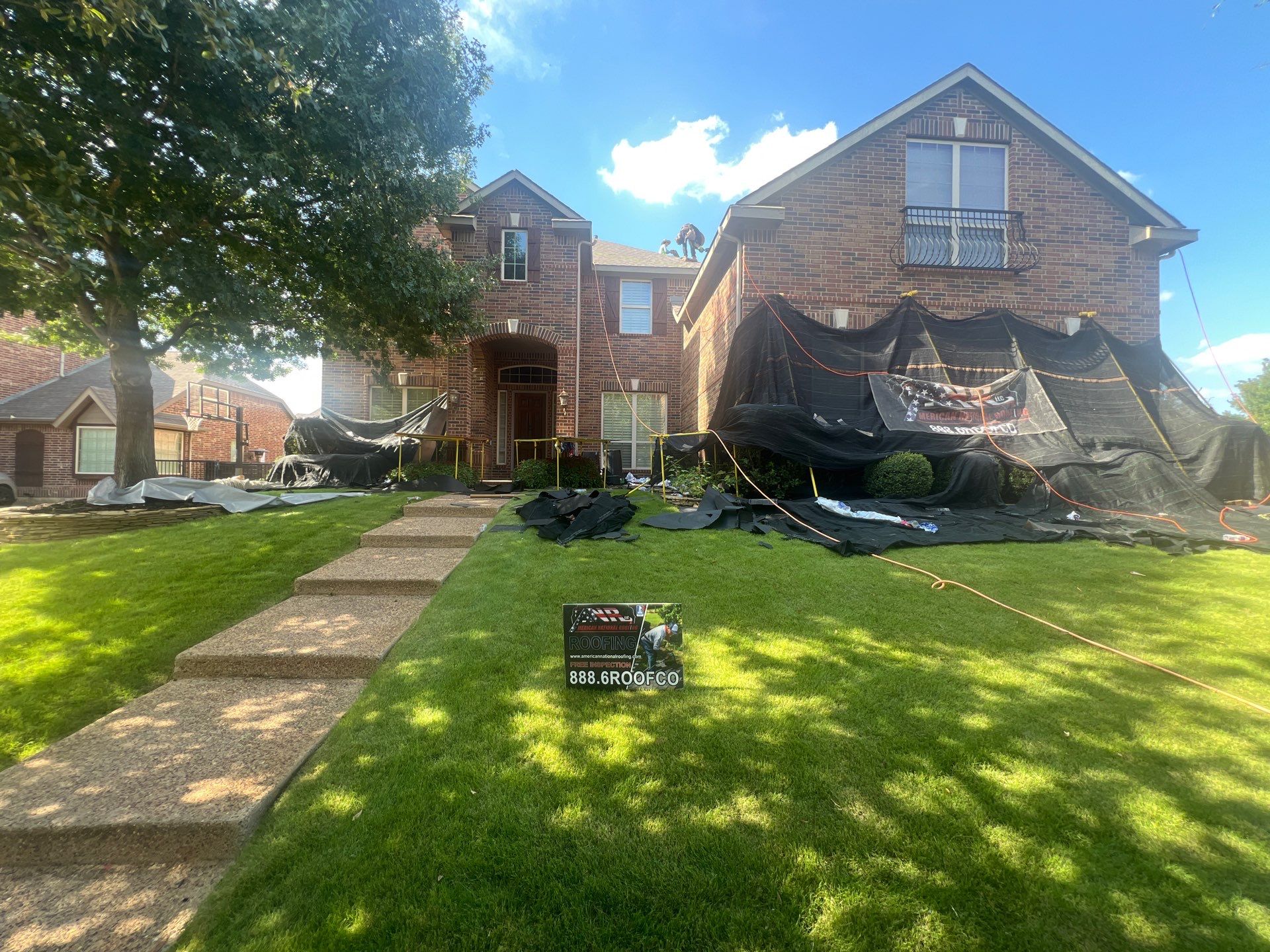 House during roofing work with an American National Roofing yard sign and protected flowers and windows.
