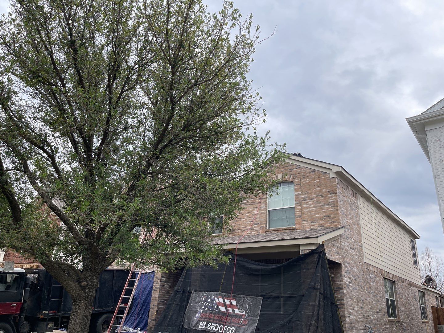 Ground-level view of a home during hail damage roof repair with the windows covered and protected and an American National Roofing sign posted