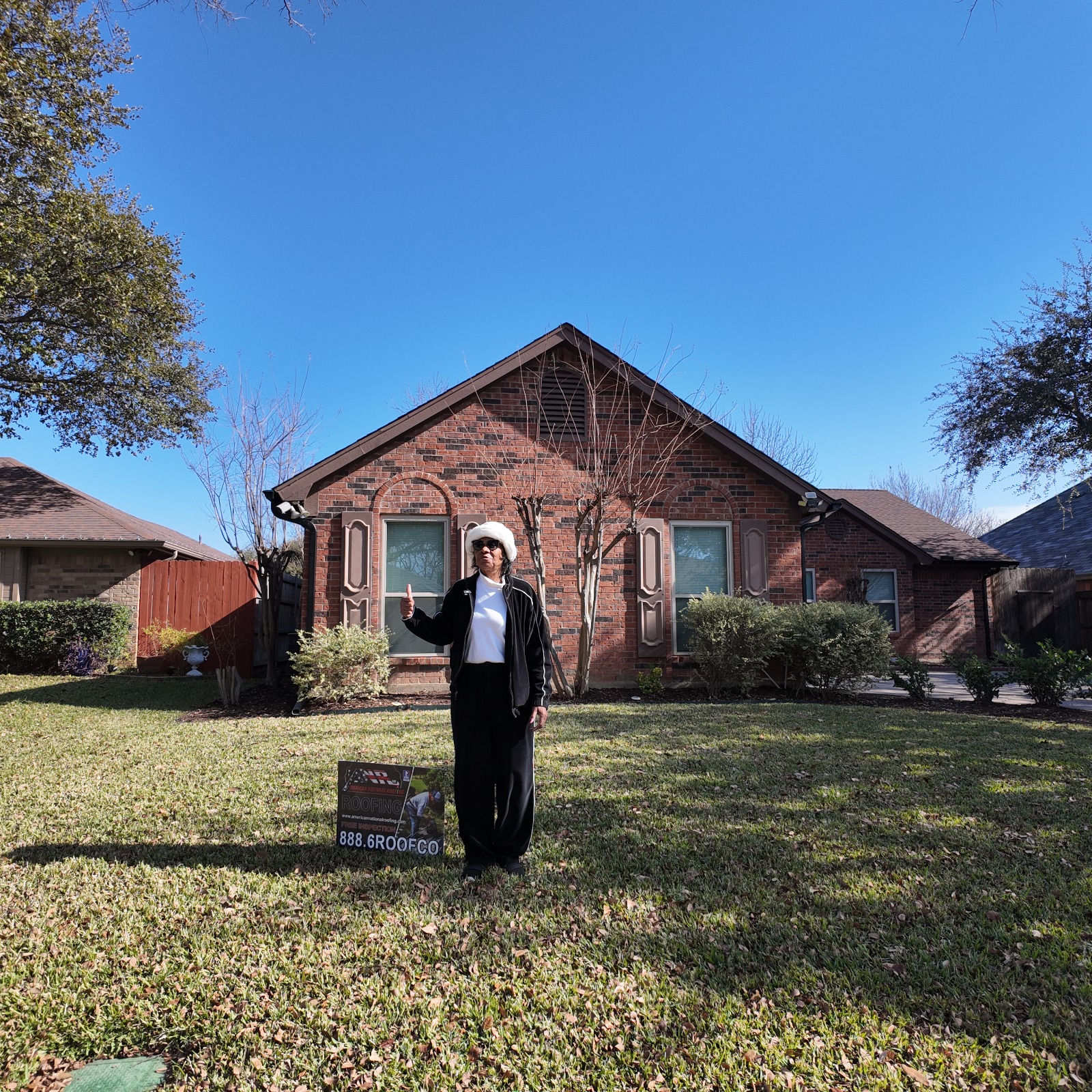 Happy homeowner giving a thumbs up in front of her new roof next to the American National Roofing yard sign